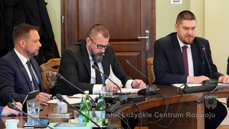 trzech mężczyzn w garniturach, siedzą przy stole